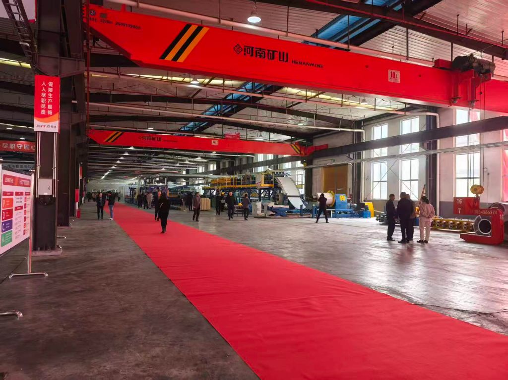 车间内铺有红色迎宾地毯，两侧是现代化夹芯板自动化生产线，上方悬挂 “河南矿山” 品牌红色行车，工业氛围浓厚